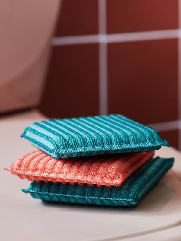 Egy fürdőszobában három különböző színű PEPPRIG szivacsot látunk egymásra pakolva.