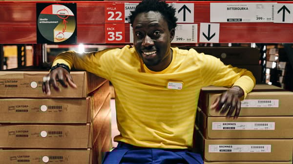 Egy IKEA dolgozó a termékek közt ül az önkiszolgáló raktárban.