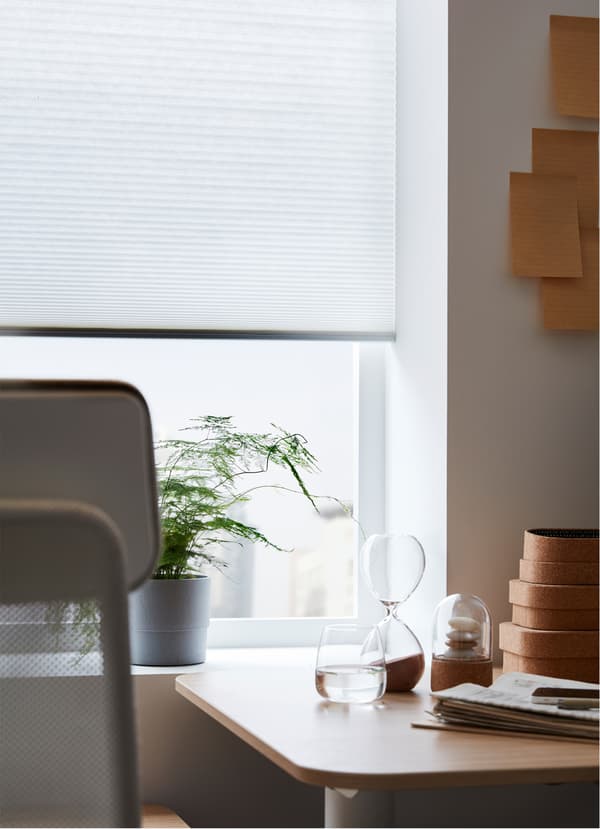Egy IKEA HOPPVALS árnyékoló méhsejt szerkezettel, egy ablak előtt, az íróasztal és a szék mögött.