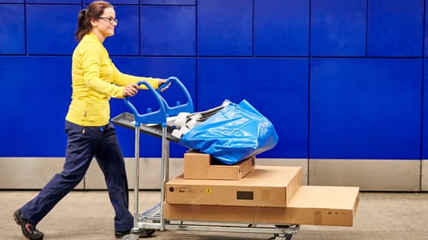 Egy IKEA munkatárs egy telepakolt bevásárlókocsit tol.