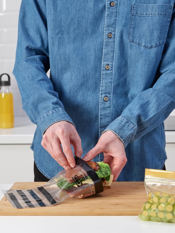 Egy kék inges ember szendvicset pakol az ISTAD zacskóba, míg a mellette látható másik zacskóba fehér szőlő került.