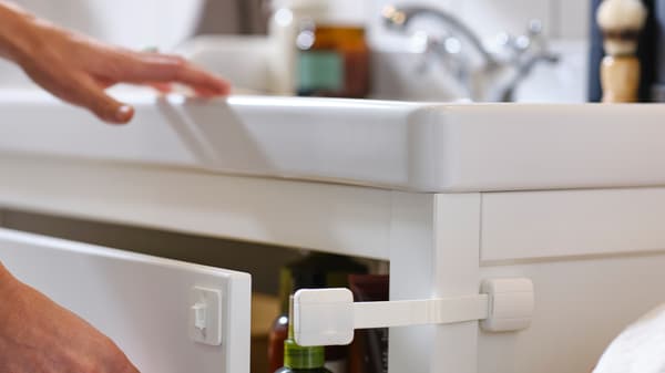 Egy kéz kihúzza egy fehér HEMNES mosdóállvány fiókját, amelyhez egy fehér UNDVIKA többfunkciós zár van rögzítve.