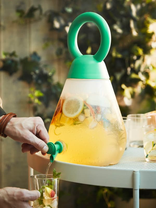 Egy kezet látunk, amint éppen gyümölcsös itallal tölti meg a poharát a SOMMARFLOX csapos italadagolóból.