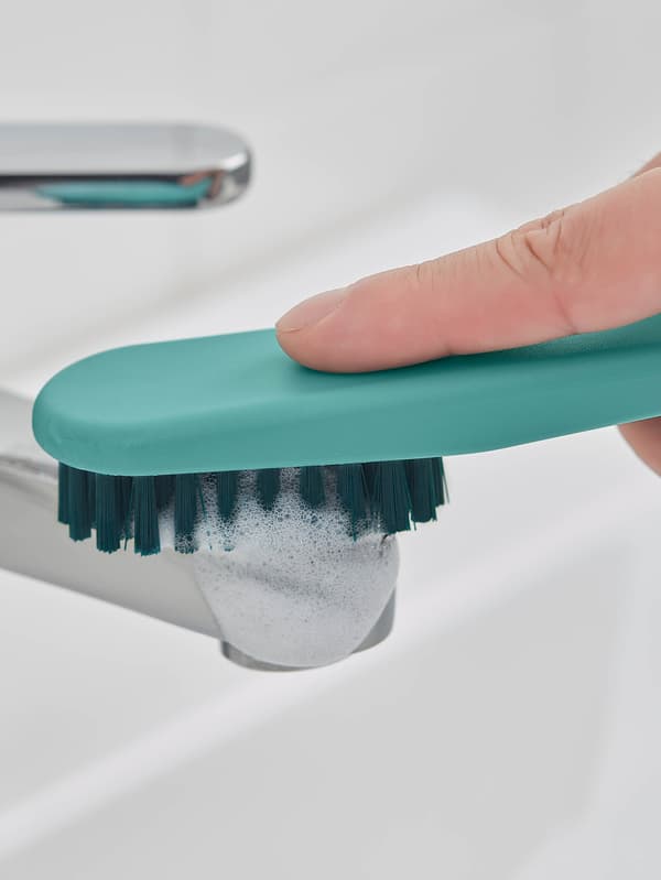 Egy kezet látunk, amint türkiz PEPPRIG kefével súrolja a fürdőszobai csapot. 