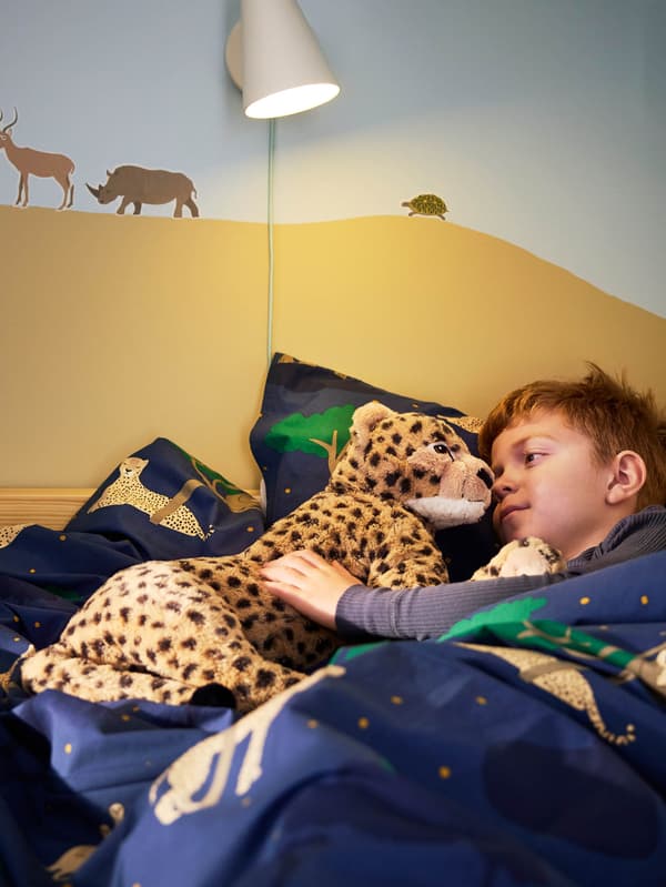 Egy kisfiú SANDLÖPARE puha játék gepárdot tart a karjaiban.