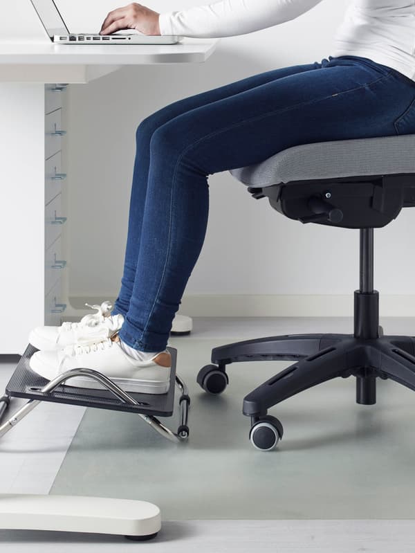 Egy lány a laptopján dolgozik egy fehér asztal mellett, lába pedig fekete DAGOTTO lábtar-tón pihen.