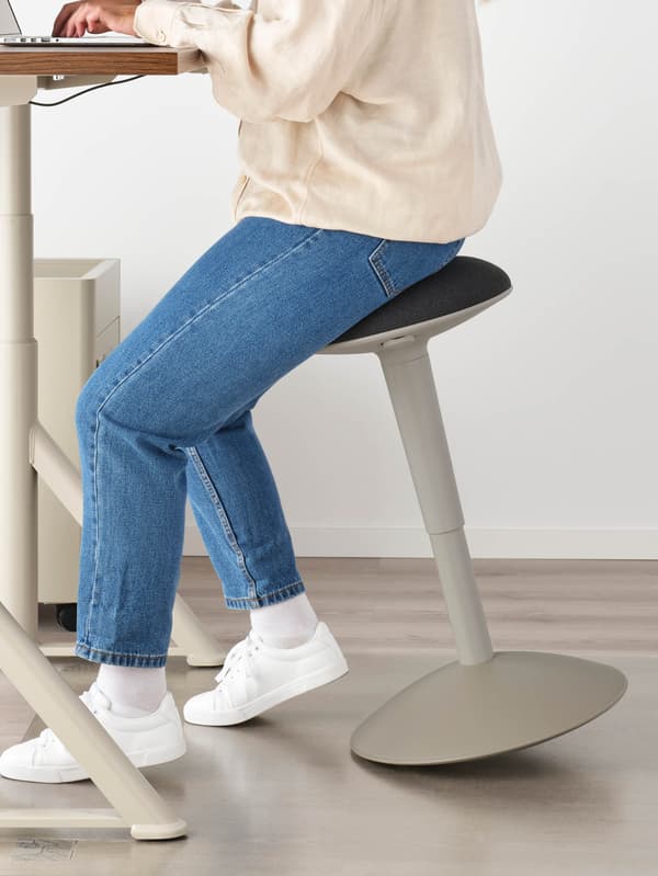 Egy lány ül egy NILSERIK ülőkén egy állítható magasságú IDÅSEN íróasztalnál, és éppen a laptopján dolgozik.