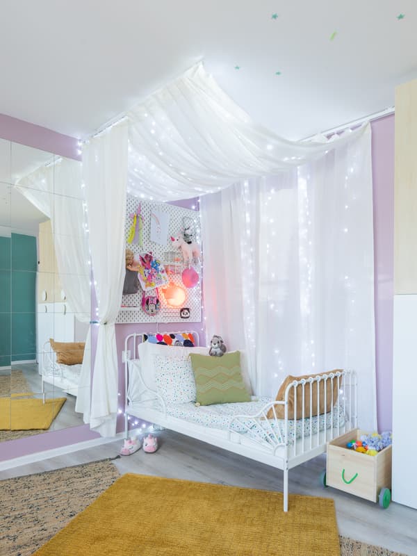 Egy lánygyerek számára kialakított alvósarkot látunk fehér ággyal és baldachinnal kiegészítve.