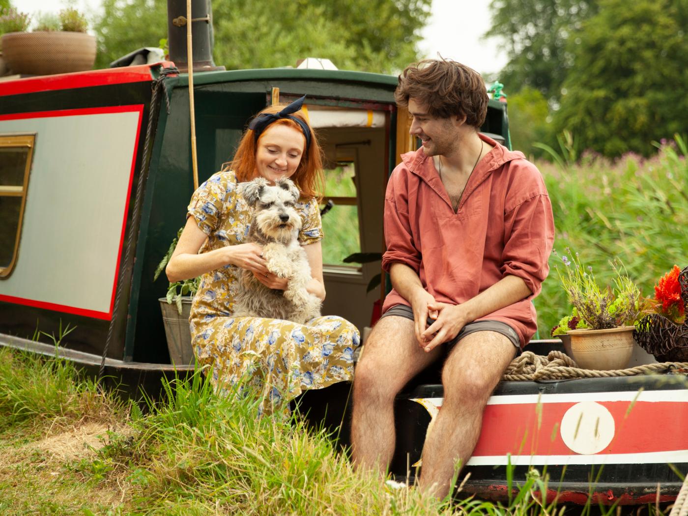 Egy nő, egy férfi és egy kis kutya egy lakóhajó fedélzetén pihen.