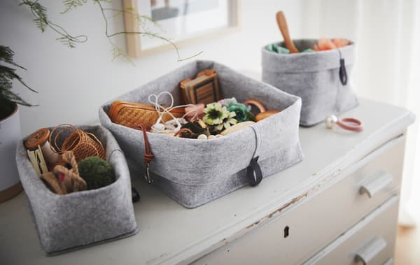 Egy régi, kopott fiókos szekrényen egy RAGGISAR textil kosárkészlet áll, a kosarakban mindenféle apró kis tárgy van. 