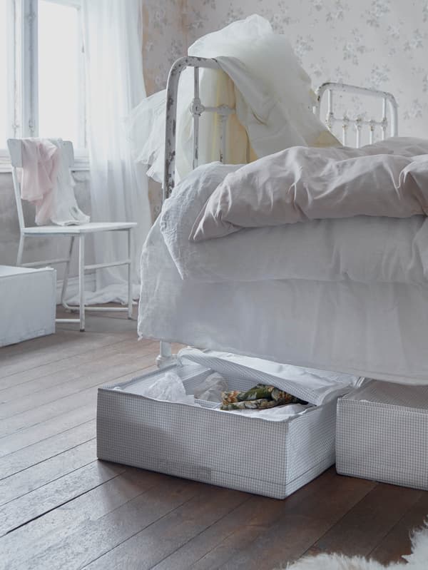 Egy romantikus hálószobában egy szürke/fehér STUK tárolót látunk egy fehér ágy alatt.