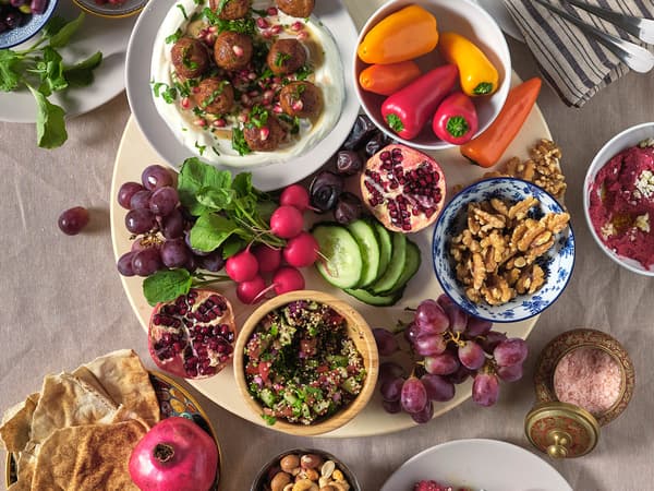Egy SNUDDA forgótálcán húsmentes HUVUDROLL golyók burgonyapüré körettel, kis tálkákban paprika, retek, szőlő, gránátalma és diófélék. Körben, további tányérokon több más étel látható.