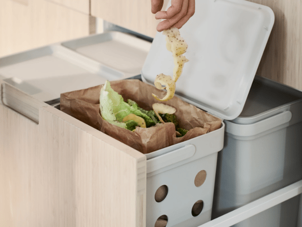 Egy szelektav szemétgyűjtőbe élelmiszerhulladékot dob egy kéz.