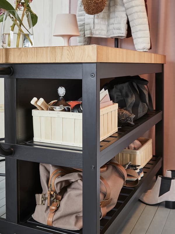 Egy táskák és egyebek tárolására használt fekete tölgy IKEA VADHOLMA konyhasziget egy előszobában.
