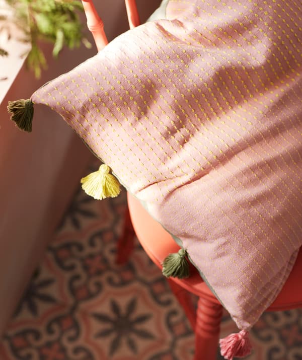 Ei solstenket pute i en rød trestol. KLARAFINA putetrekk har broderte linjer og dusker i forskjellige farger.