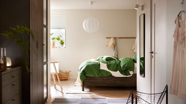 Ei TONSTAD seng med oppbevaringsrom i brunbeiset eikefiner med KUNGSCISSUS sengetøy står under ei hvit REGNSKUR taklampe.