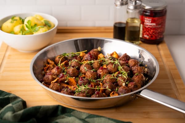 Eierschwammerln, Köttbullar & Preiselbeer-Glasur in einer Pfanne präsentiert.