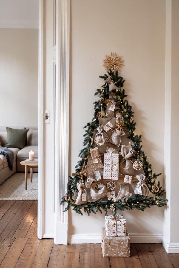 Ein Adventskalender im natürlichen Look wurde mit Kindern gebastelt. Ein Tannenbaum hängt mit bunten Kugeln an einer weißen Wand.