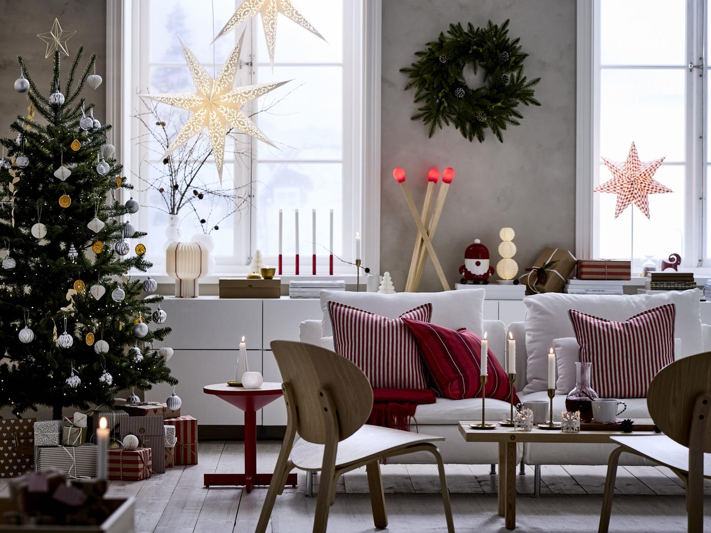 Ein Ausschnitt eines Wohnzimmers, weihnachtlich festlich geschmückt, mit Weihnachtsbaum, Fenster-Dekoration und jeder Menge Lichtern. 