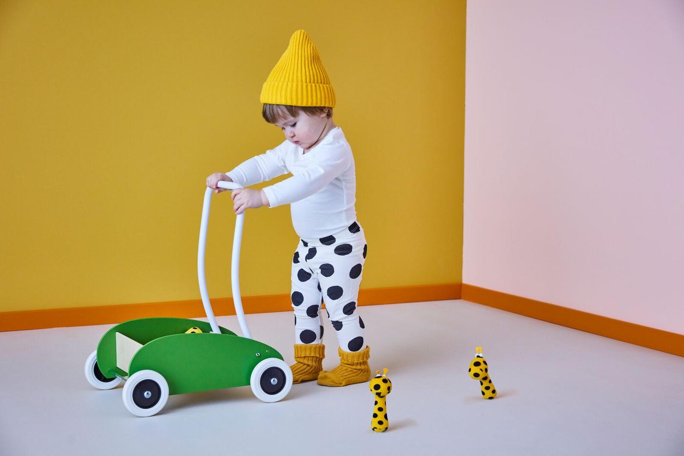 Ein Baby fährt einen grünen Holzwagen in einem bunten Studio