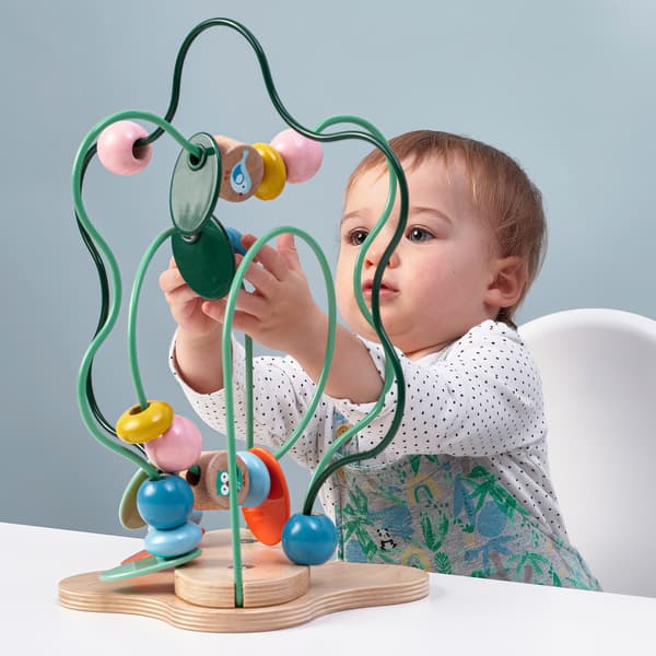Ein Baby sitzt auf einem Stuhl an einem Tisch auf dem die UPPSTÅ Motorikschleife steht und spielt damit.
