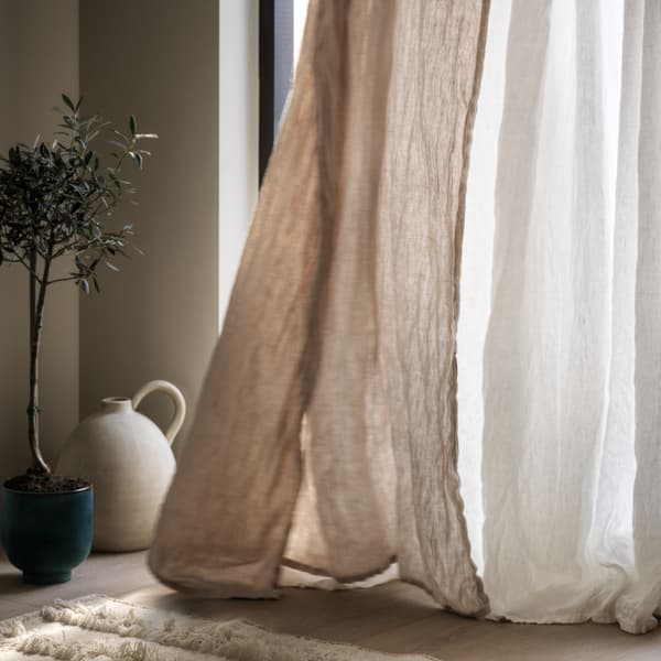 Ein beigefarbener Gardine und ein weisser SILVERLÖNN Gardinenstore bewegen sich vor einem Fenster im Wind.