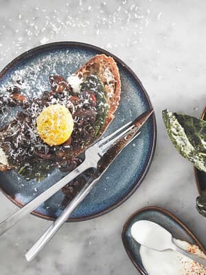 Ein belegtes Brot und Besteck auf einem blauen Teller.