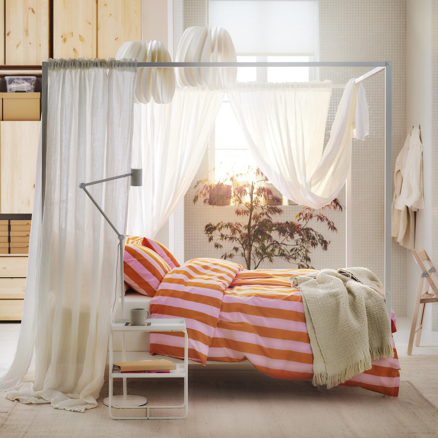 Ein Bett mit orange-rosa Bettwäsche steht mitten in einem Raum.