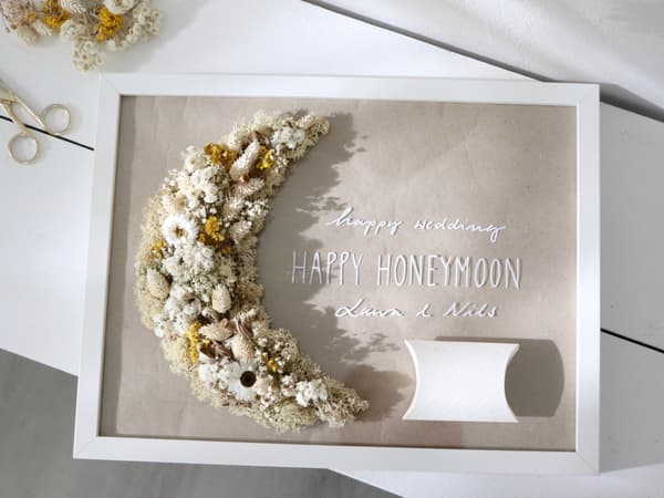 Ein Bilderrahmen mit einem aufgeklebtem Trockenblumengesteckt, einem persönlichem Gruß und einem kleinen aufgeklebtem Päckchen für das Geldgeschenk. 