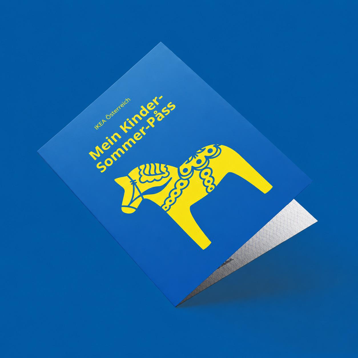 Ein blaues Heft mit der Aufschrift „IKEA Österreich – Mein Kinder-Sommer-Pass“ und einer gelben Dala-Pferd-Illustration schwebt vor einem blauen Hintergrund.
