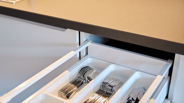 Ein Büroraum mit schwarzen Schreibtischen zum Sitzen oder Stehen. Zwei Mitarbeitende besprechen sich.