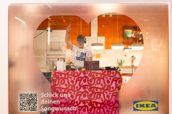 Ein DJ steht hinter einem mit Herz dekorierten DJ-Pult und nimmt Songwünsche entgegen.

