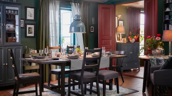 Ein dunkel gestaltetes Esszimmer mit einem Ausziehtisch und fünf Stühlen in Schwarz sowie einem Teppich mit orientalischem Muster.