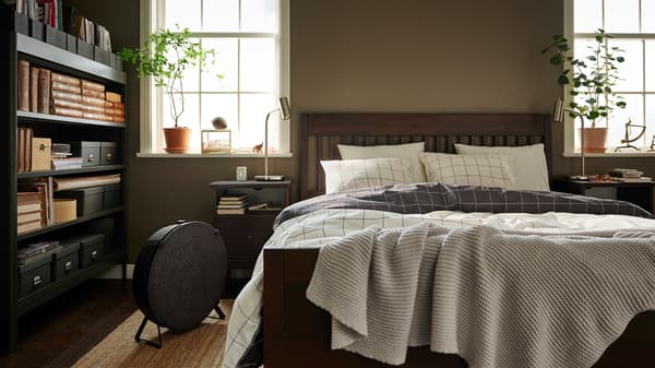 Ein dunkelbraunes IDANÄS Bettgestell mit VITKLÖVER Bettwäsche auf einem naturfarbenen LOHALS Teppich in einem aufgeräumten Schlafzimmer.