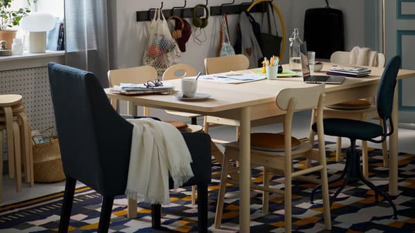 Ein Essbereich mit einem RÖNNINGE Tisch. Darauf stehen verschiedene Gegenstände. Umgeben ist der Tisch u. a. von RÖNNINGE Stühlen auf einem TÅRBÄK Teppich.