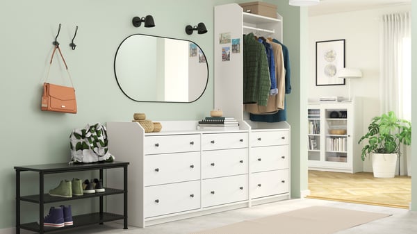 Ein Flur mit einer weißen HAUGA Kombination aus einer Kommode mit sechs Schubladen und einem offenen Kleiderschrank mit drei Schubladen. Im Wohnzimmer daneben steht eine weiße HAUGA Vitrine.