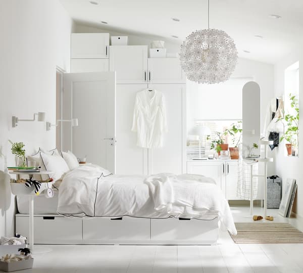 Ein freundliches, weißes Schlafzimmer mit einem weißen Kleiderschrank, Kleiderständer und Wandleuchte.