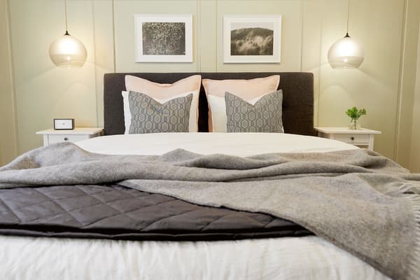 Ein frisch gemachtes Bett im Schlafzimmer mit verschiedenen Kissen, daneben Nachttische und darüber Beleuchtung