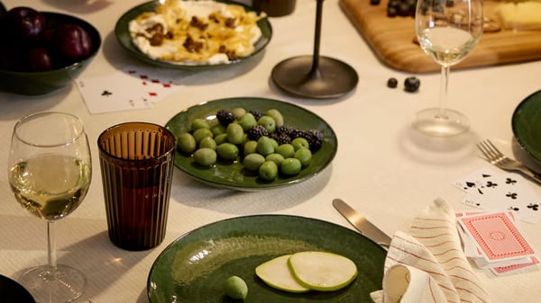 Ein gedeckter Tisch mit Oliven und anderen Speisen auf Tellern, Weingläser und einem Kartenspiel
