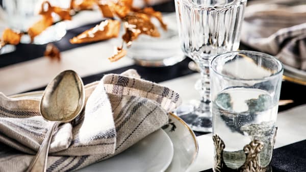 Ein gedeckter Tisch mit zwei Gläsern rechts und auf einem Teller liegen eine Serviette und ein Löffel.