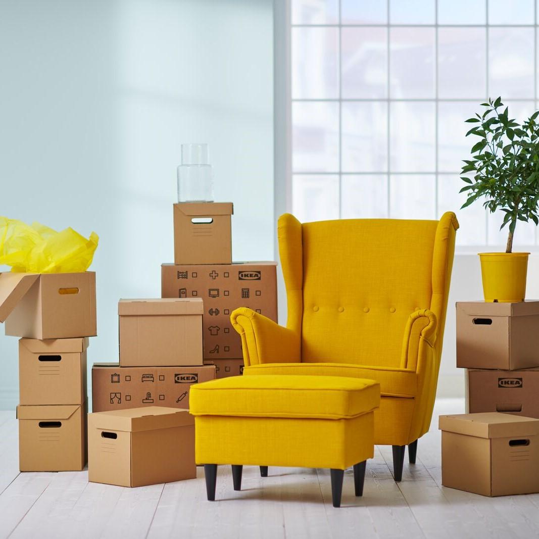 Ein gelber Strandmon Sessel steht zwischen vielen IKEA Umzugsboxen in einem hellen Raum.