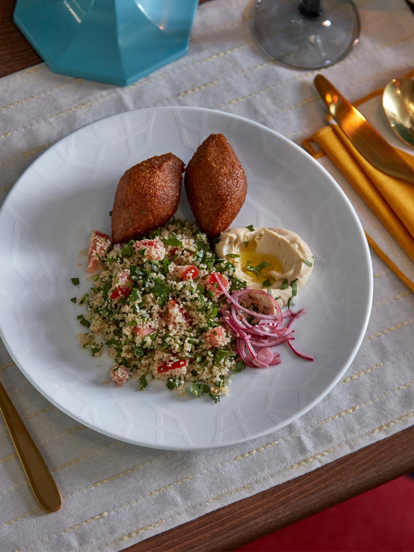 Ein GOKVÄLLÅ Teller mit Besteck und ein Glas befinden sich auf einem beigefarbenen GOKVÄLLÅ Tischset. Auf dem Teller ist eine leckere Speise angerichtet.