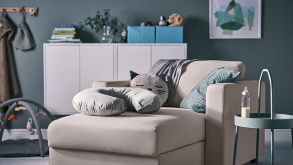 Ein graues LEN Stillkissen liegt auf einer VIMLE Récamiere in Beige. Daneben befindet sich ein BURVIK Beistelltisch in hellem Graugrün mit einem Fläschchen.