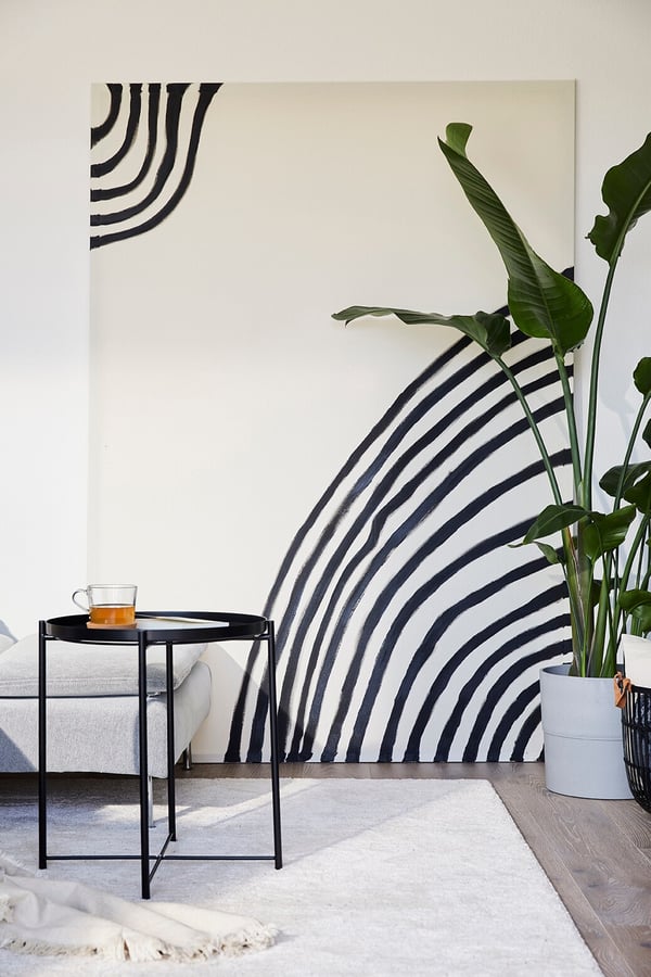 Ein grossen Bild mit abstrakten Linien steht auf dem Boden eines Zimmers und lehnt an der Wand