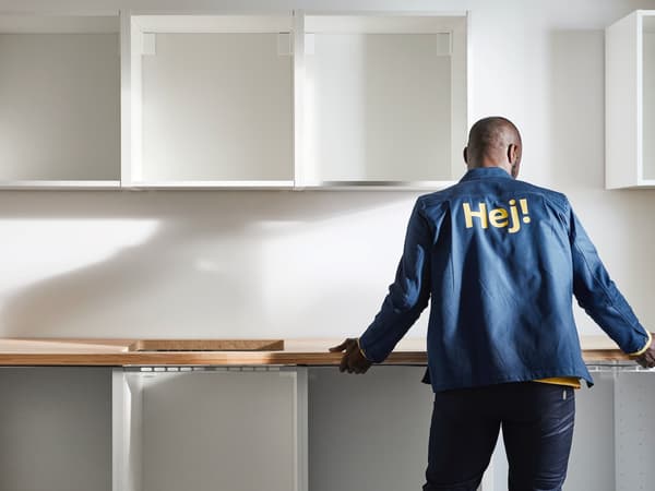 Ein Handwerker montiert eine Arbeitsplatte auf bereits an der Wand angebrachten Küchen-Unterschränken. An der Wand hängt eine Reihe leerer Wandschrank-Korpusse