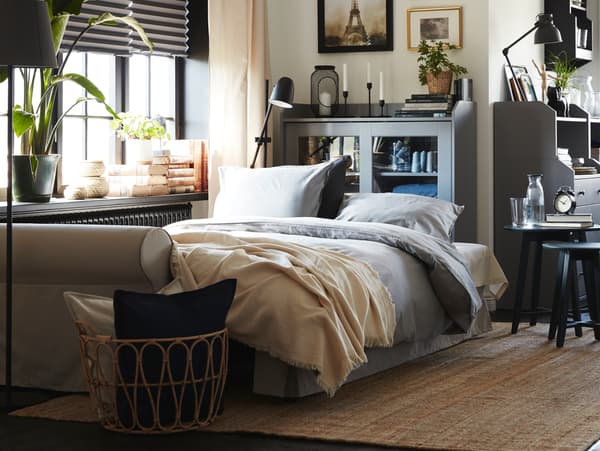 Ein hellbeiges Bettsofa mit dem ÄNGSLILJA Bettwäscheset. Dahinter befindet sich eine Vitrine an der Wand. 