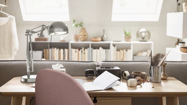 Ein Homeoffice mit einem LISABO Schreibtisch aus Eschenfurnier hinter einem Sofa, einer FORSÅ Arbeitsleuchte und einem GUNNARED Drehstuhl.