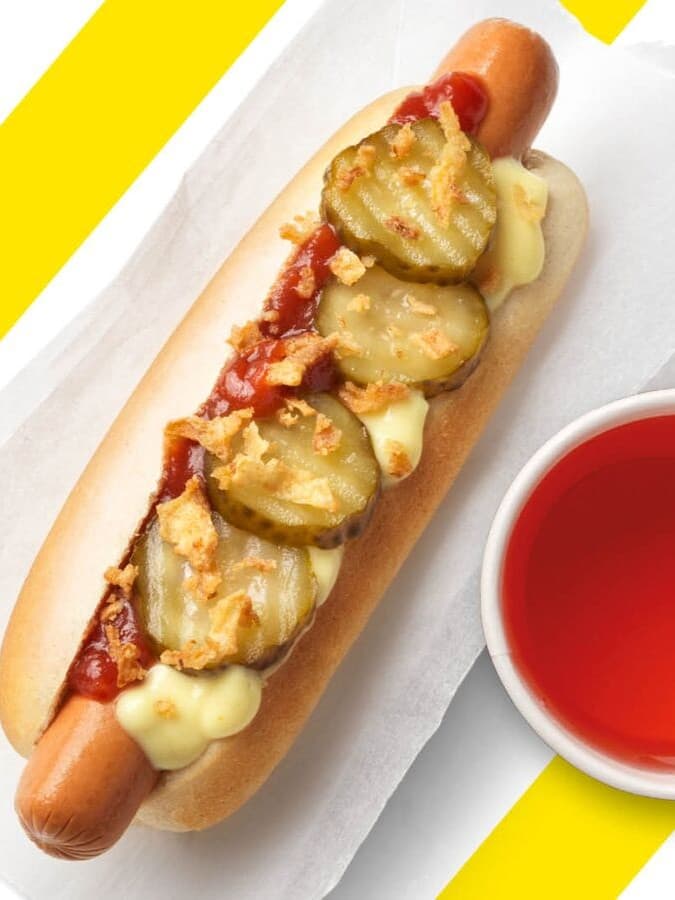 Ein Hot Dog und ein Schwedenkracherl vor einem gelb-weiß gestreiftem Hintergrund.