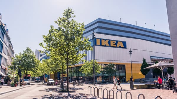 Ein IKEA Einrichtungshaus steht hiner Bäumen und Fußgänger*innen laufen davor.