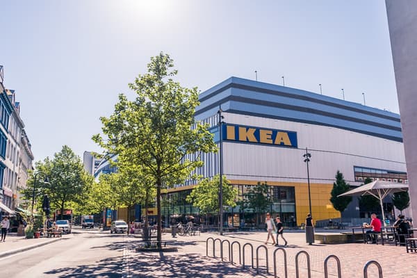 Ein IKEA Einrichtungshaus steht hiner Bäumen und Fußgänger*innen laufen davor.